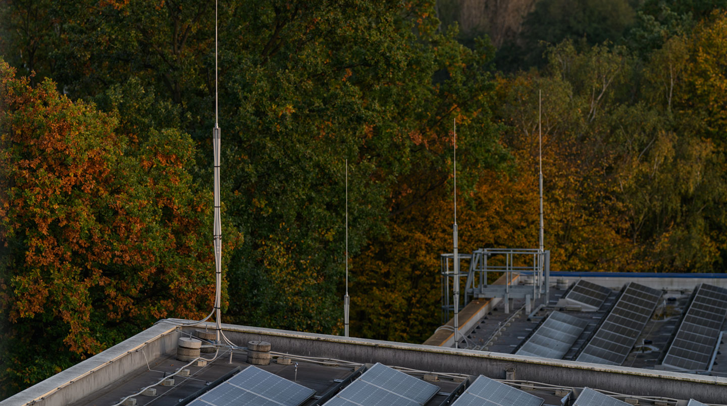 External photograph of UK industrial building roofline showing installed lightning protection system with Franklin rod air termination, copper down conductors with standoff brackets, and visible earthing connections—demonstrating layered protection component integration
